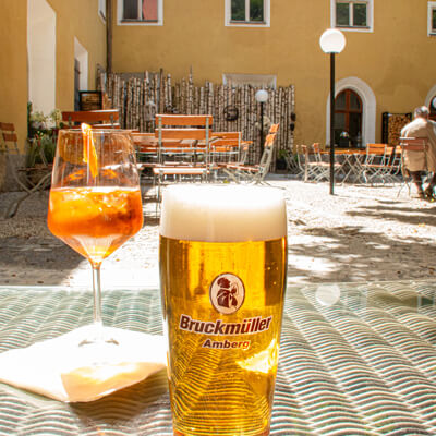 Ein Glas Bier und Aperol Spritz stehen auf einem Tisch im Klostergarten.