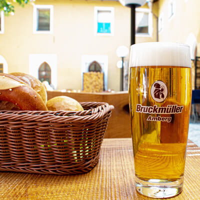 Ein Korb mit Brezen und Brötchen und einem Glas Bier stehen auf einem Holztisch.